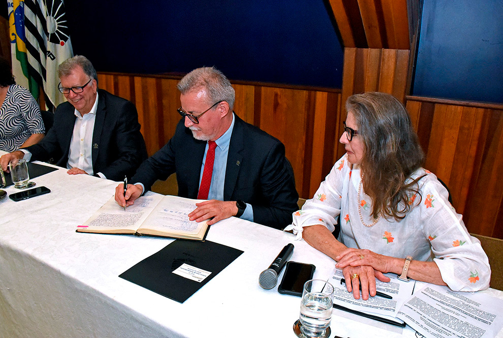 pessoas sentadas em volta de uma mesa, assinando documento